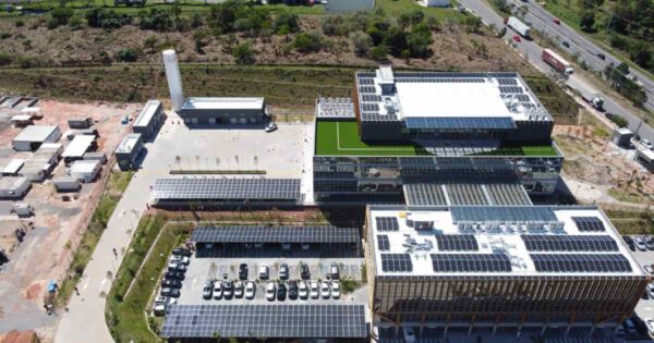 Vista aérea de edifício corporativo com painéis solares instalados no telhado e em estruturas de estacionamento, representando projeto de energia solar para empresa de grande porte.