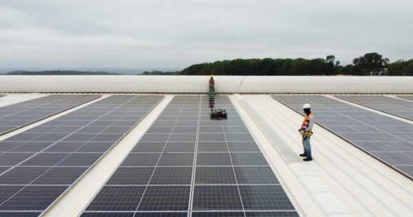 Técnicos realizando limpeza e inspeção de painéis solares instalados em telhado industrial, durante operação e manutenção de usina fotovoltaica.