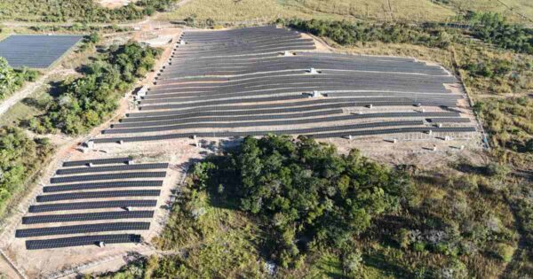 Vista aérea de usina solar de grande porte instalada em área aberta, com fileiras de módulos fotovoltaicos organizados para geração distribuída empresarial.