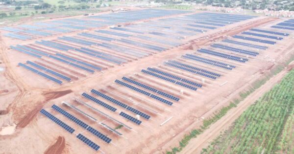 Vista aérea de fazenda solar com múltiplas fileiras de painéis fotovoltaicos instalados em solo, representando projeto de geração compartilhada no Brasil.