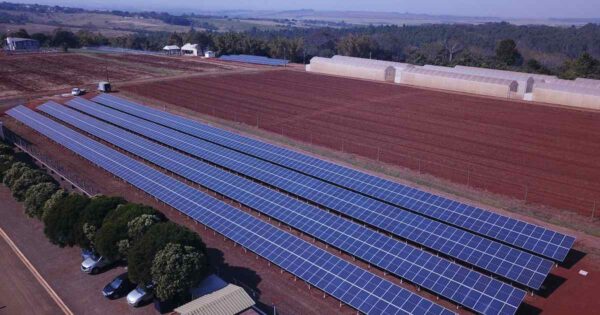 Vista aérea de usina solar instalada em área rural com fileiras de painéis fotovoltaicos sobre estrutura fixa no solo.
